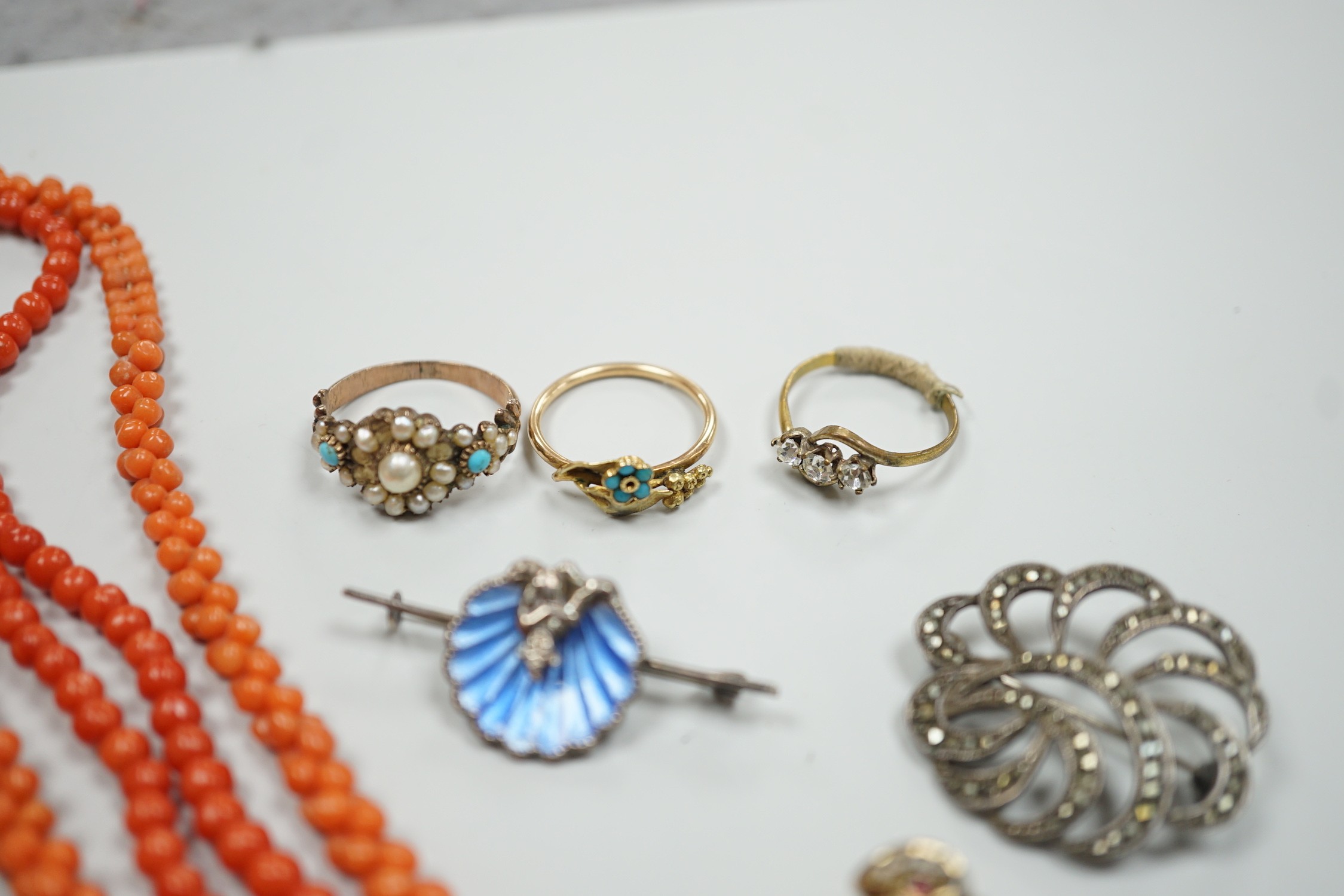 A yellow metal, seed pearl and red stone set 'bird on a branch' brooch, width 30mm, two coral bead necklaces, an enamelled white metal imp and shell brooch, three rings, a marcasite brooch and a simulated pearl necklace.